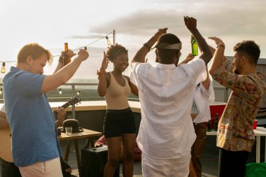 Çatı partisinde coşkulu kültürler arası arkadaşlar dans ediyor.