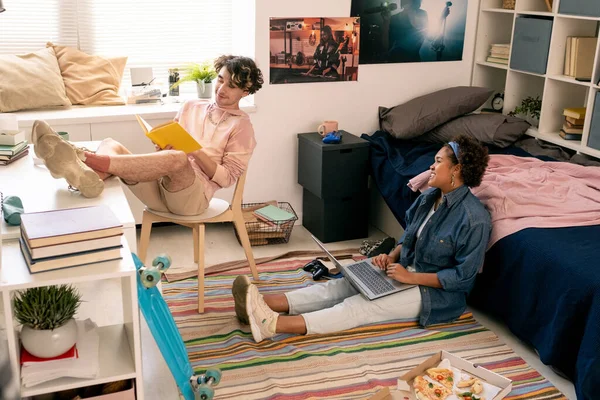 Two teenagers reading book and using laptop in bedroom — Stock Photo, Image