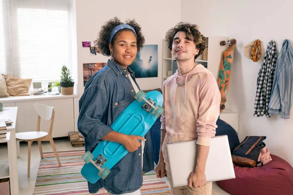 与滑板和笔记本电脑站在卧室的快乐的跨文化夫妇 — 图库照片