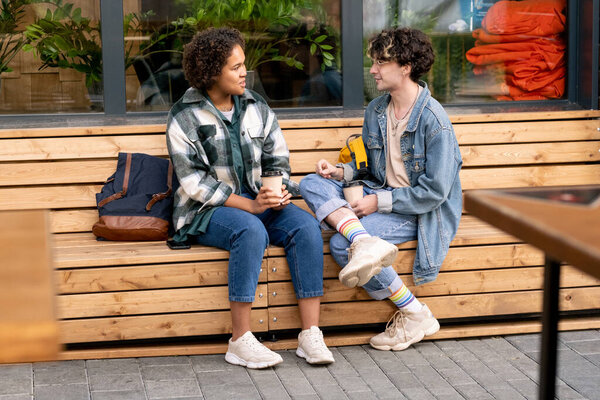 Cute teenage girl and her boyfriend having drinks on wooden bench