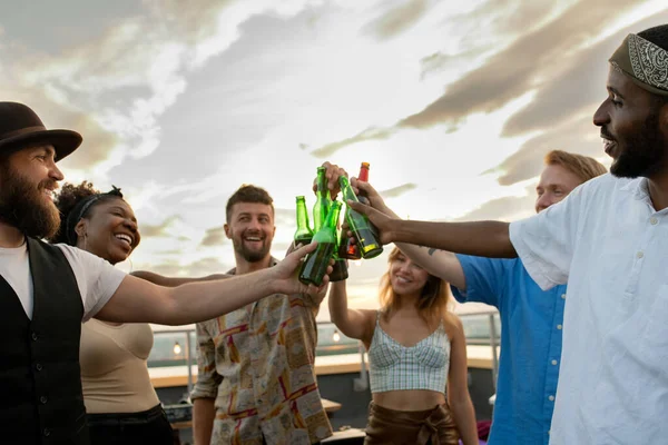 Jóvenes multirraciales felices brindando con botellas de cerveza en la fiesta —  Fotos de Stock