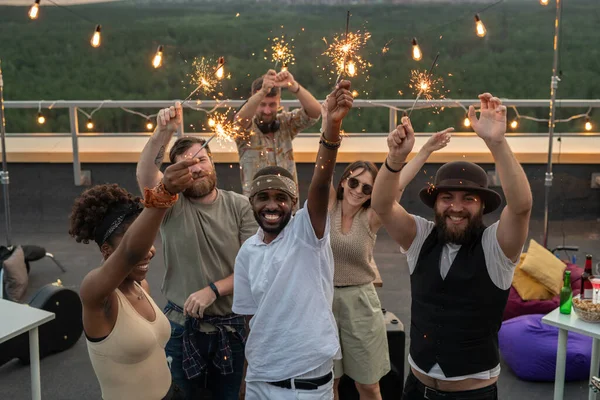 Jóvenes amigos felices con brazos levantados bailando con luces de bengala —  Fotos de Stock