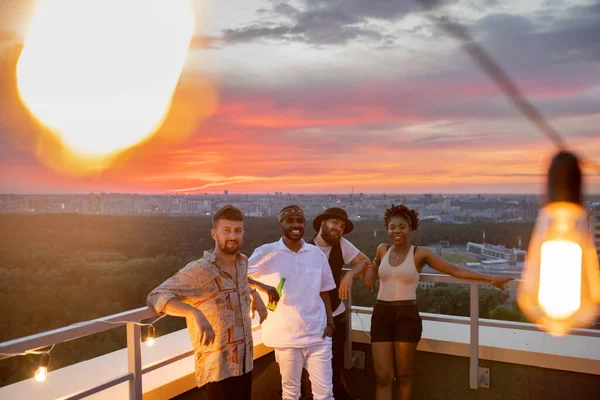 Vier glückliche junge Freunde stehen auf Dachterrasse gegen Stadtbild — Stockfoto