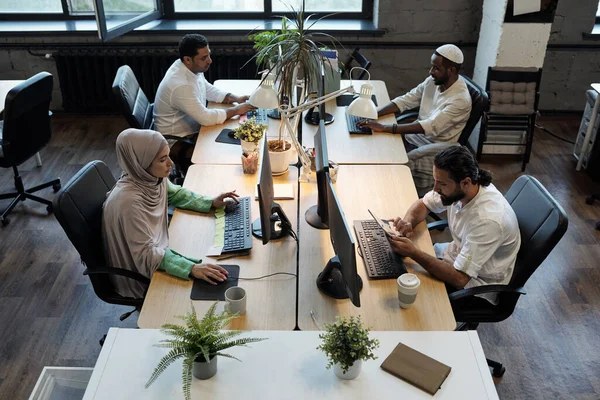 Quatro jovens colegas de trabalho sentados à mesa em frente aos computadores — Fotografia de Stock