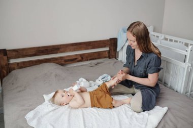 Dikkatli ol, genç anne. Yatağa oturmuş, oğlanın bacaklarına masaj yapıyor.