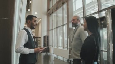 Resepsiyona kadar onlara eşlik eden ve kibarca iletişim kuran üniformalı konuklara otel lobisinde hoş geldin diyen genç erkek kapıcının yavaş çekimleri.