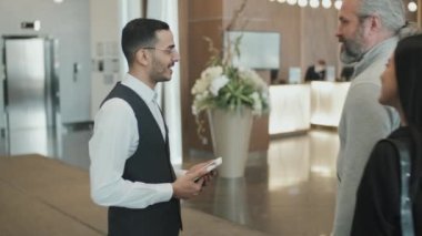 Otel lobisinde onlara resepsiyona kadar eşlik eden modern misafir çifti ağırlayan kibar erkek kapıcının yavaş çekimleri.