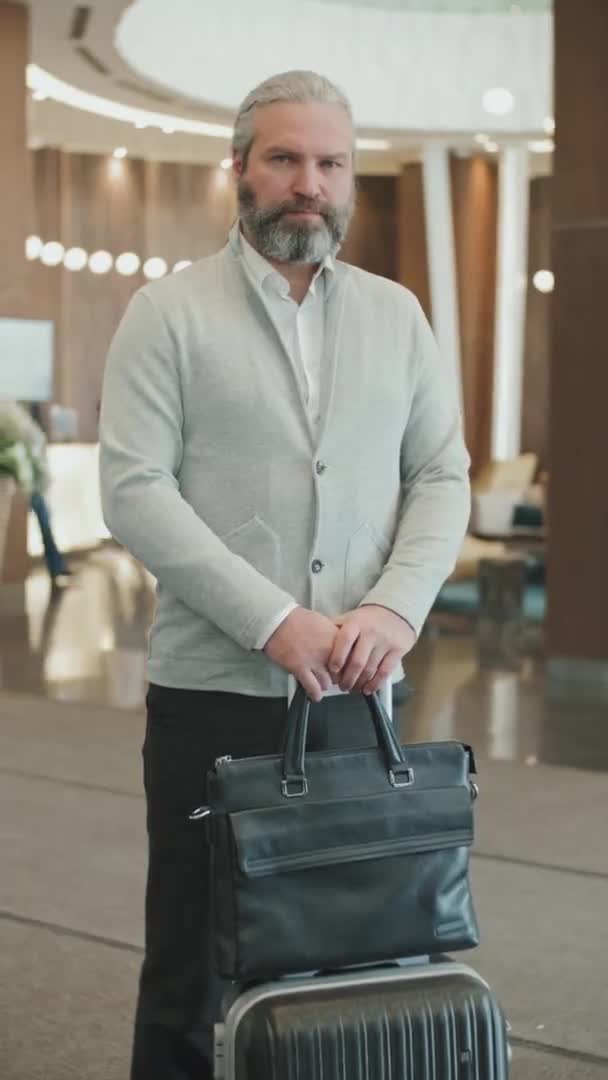 在时髦的现代酒店大堂里 穿着智能便服 背着行李 自信而成熟的商人的垂直中速肖像在镜头前出现 — 图库视频影像