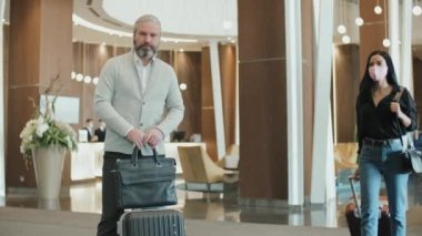 Modern otel lobisinde kameraya poz veren olgun sakallı iş adamının orta yavaş portresi.