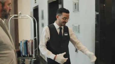 Yetişkin bir iş adamına otel odasına kadar eşlik eden, bavulunu birlikte asansöre binerken orta boy bir fotoğraf.