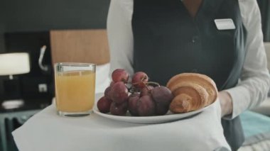 Modern otel odasında, elinde taze lezzetli bir kahvaltı tepsisiyle tanınmayan bir garsonun yavaş yavaş göbeğine yakın çekim.