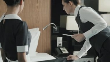 Kadın otel müdürünün ya da denetçi kontrol odasının orta ölçekli görüntüsü yüksek standartlarda temizlenmiş, temizlikçi işi kontrol ediliyor ve kusurlara işaret ediliyor