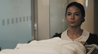 Otel koridorunda havluları ve çarşafları taşıyan el arabasıyla yürüyen güzel esmer hizmetçi.