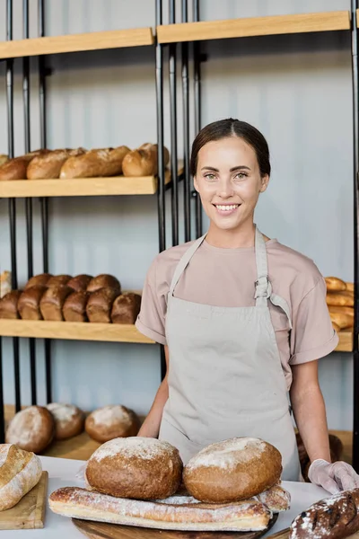 Счастливая пекарь, стоящая на рабочем месте и продающая свежий хлеб — стоковое фото