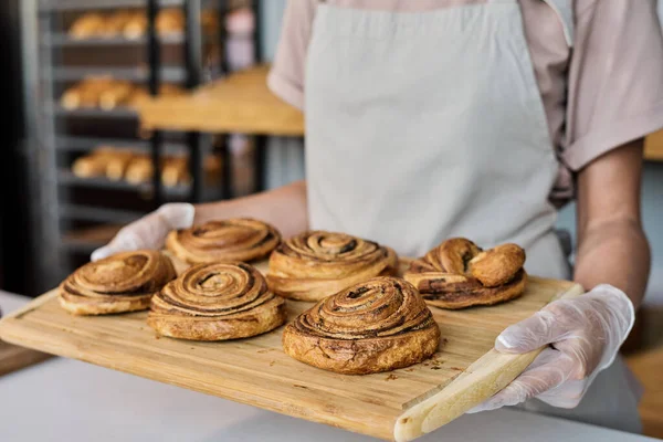 Пекарь в перчатках несет поднос со свежими булочками — стоковое фото