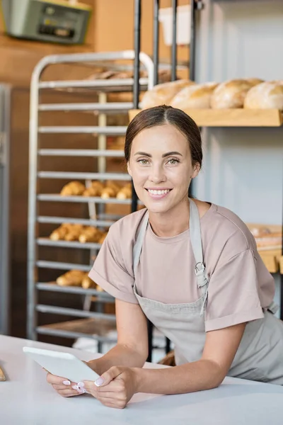 Bastante trabajador de panadería con la tableta de flexión sobre el lugar de trabajo — Foto de Stock