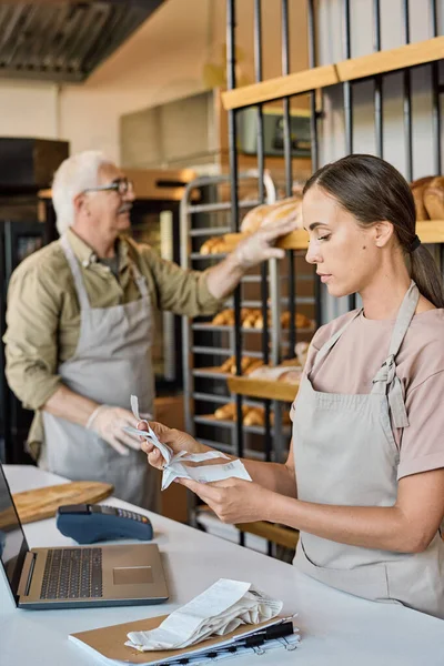 Upptagen kvinnlig arbetare i bageri tittar igenom receits — Stockfoto