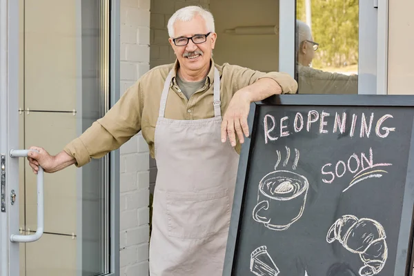 Glücklicher älterer Bäckereibesitzer steht am Eingang und öffnet Tür — Stockfoto