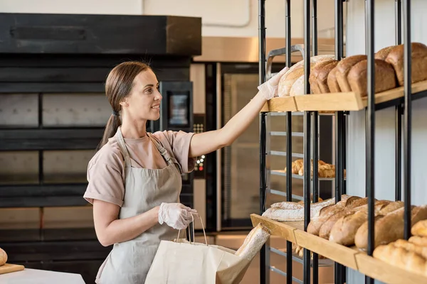 진열품에서 신선 한 빵을 먹는 여성 제빵사나 서기 — 스톡 사진