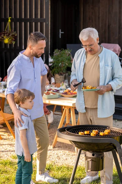 Volwassen man, zijn zoon en kleinzoon maken gegrilde maïs voor familie diner — Stockfoto