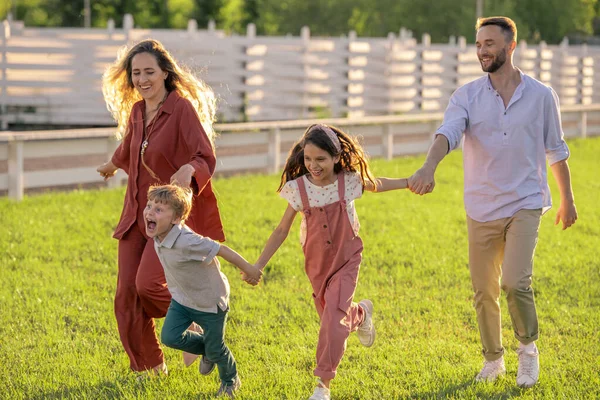 Glada unga par och deras två barn springer ner grön gräsmatta — Stockfoto