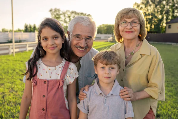 Großeltern mit Brille stehen neben ihren beiden niedlichen Enkeln — Stockfoto