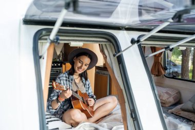 Küçük bir evde tekerlekli sandalyede oturmuş gitar çalan gülümseyen kız.