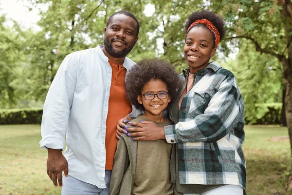 Feliz familia africana de tres mirando a la cámara en el parque —  Fotos de Stock