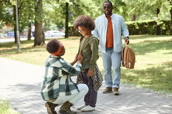 Glücklicher kleiner Junge schaut Mutter an, während Vater seinen Schulrucksack trägt — Stockfoto