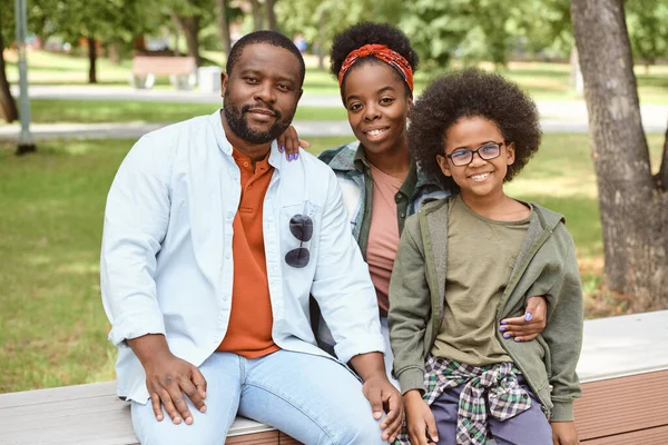 Vrolijke Afrikaanse familie zit op een bankje in het park — Stockfoto