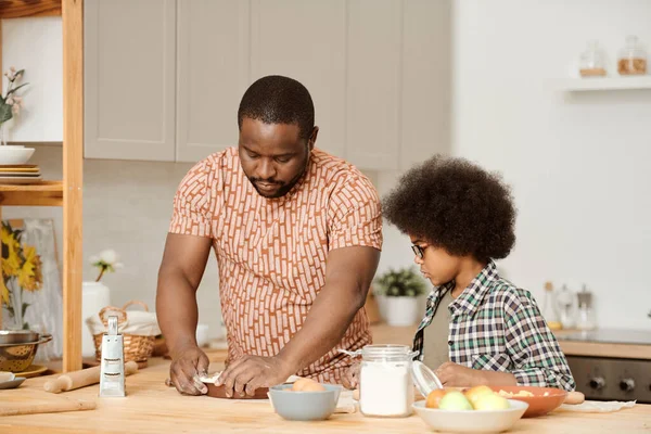 Симпатичный маленький мальчик, глядя на своего отца, кладет тесто в форму выпечки — стоковое фото