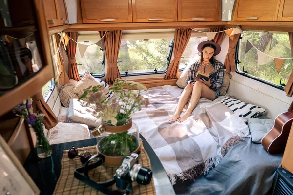 Młody zrelaksowany kobieta z otwartą książką siedzi na łóżku w domu podróży — Zdjęcie stockowe