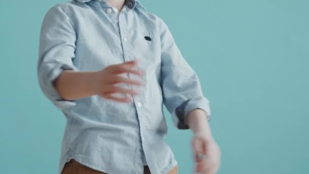6歳の男の子が腕を交差させてカメラから目をそらしながら青い背景をポーズ — ストック動画