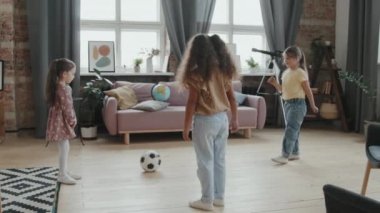 Evde oynarken rahat oturma odasında futbol oynayan 6 yaşında ve 8 yaşındaki kızların yavaş çekimleri.