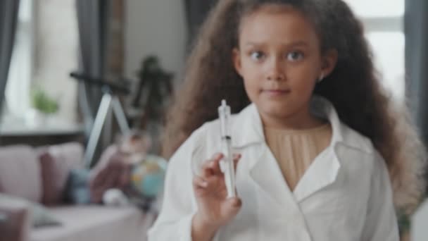 身穿白衣的8岁女孩的手持肖像 在家中摆姿势时 看着相机 并展示装有透明液体的注射器 — 图库视频影像