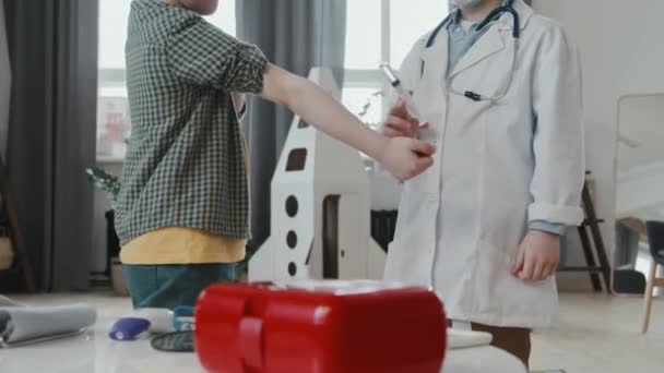 医師の衣装や顔のマスクで6歳の男の子の遅いショットを傾けるアップ自宅でプレイしながら 彼の友人にワクチンや薬を与えるふり — ストック動画