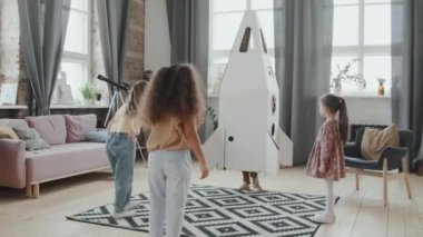 Evde karton roket modeliyle oynayan bir grup küçük çocuğun el kamerasıyla çekilmiş fotoğrafı.