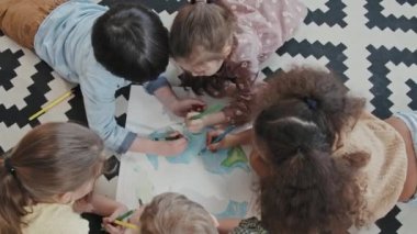 Bir grup çocuğun halının üzerinde yatıp Dünya gezegeninin boyama resimlerinin el kamerasıyla çekilmiş hali.