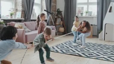 Evdeki rahat oturma odasında halat çekip halat çekme oyunu oynayan sevimli çocukların el kamerasıyla çekilmiş yavaş çekimleri.