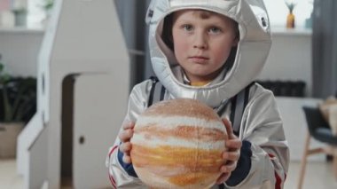 Gezegen modelini tutan ve kameraya bakan, uzay giysili yakışıklı bir çocuğun el yapımı portresi.