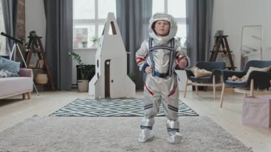 Evdeki oturma odasında kameraya poz verip selam veren 6 yaşında, güzel bir çocuğun portresi. Arka planda duran mukavva roket gemisi