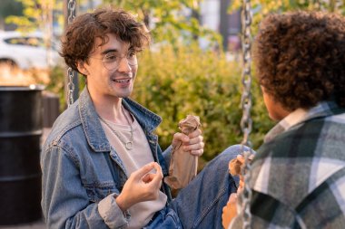 Şişeyle kağıda sarılı mutlu adam kız arkadaşıyla konuşuyor.