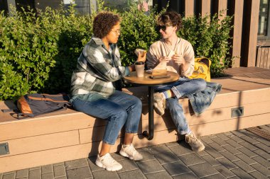 İki üniversite öğrencisi kahve ve sandviç yiyor.