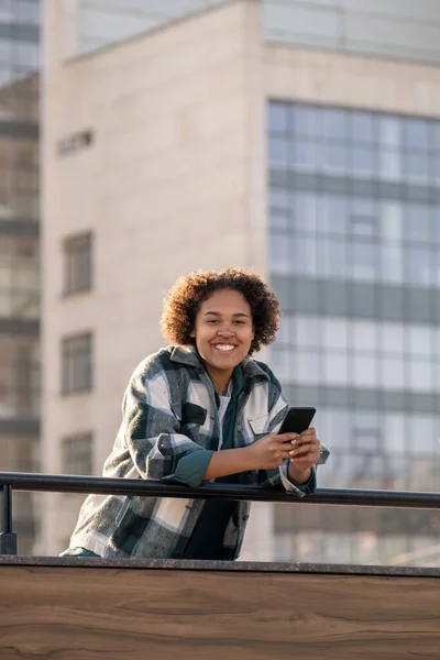 Hübscher Teenager, der dich mit zahmem Lächeln ansieht, während du das Smartphone benutzt — Stockfoto