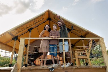 Mutlu aile, doğal ortamda glamping evinin yanında duruyor.