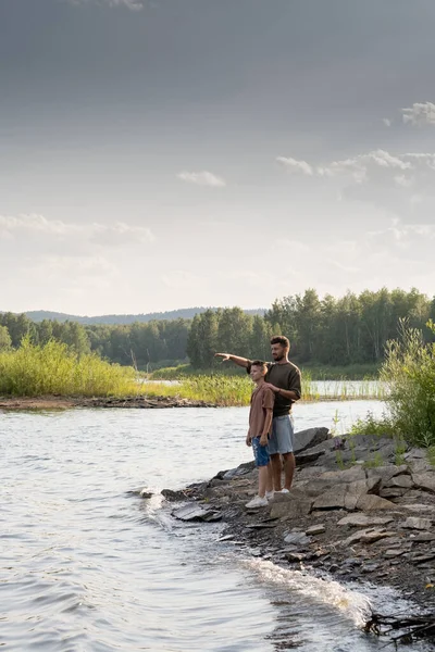 Apa és tinédzser fiú áll a vízparton a nyári pihenés alatt — Stock Fotó