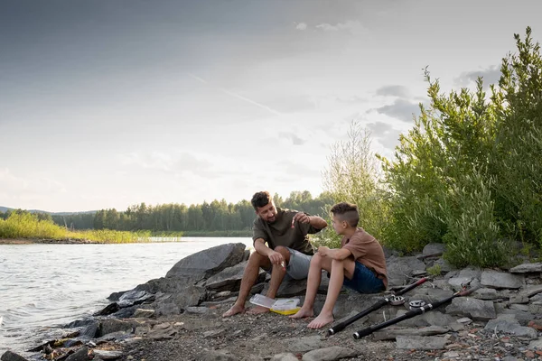 Far och son sitter framför sjön medan de fiskar — Stockfoto