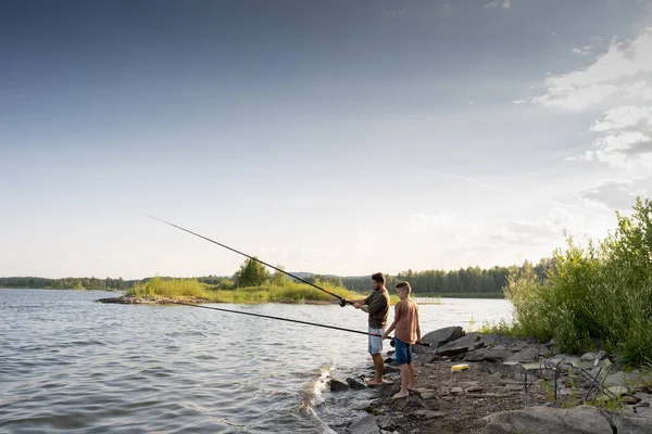 夏日，活跃的男子和十几岁的男孩带着钓竿在湖边钓鱼 — 图库照片