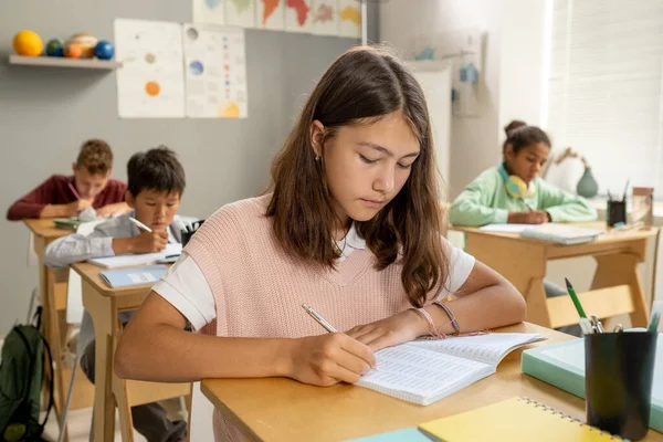 Colegiala primaria caucásica tomando notas en la lección —  Fotos de Stock