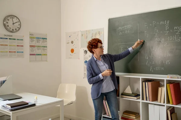 Jeune professeur de physique expliquant les formules sur tableau noir — Photo